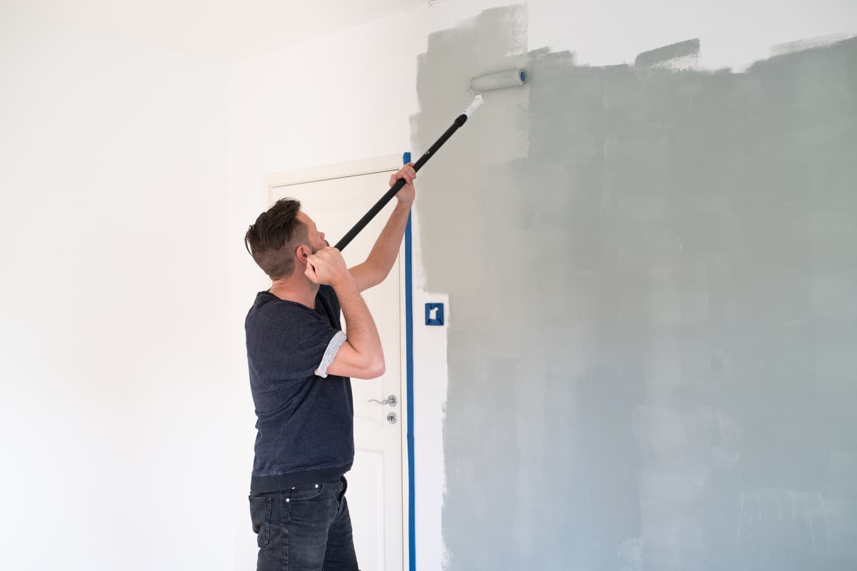 hvordan velge husmaling: en mann maler en vegg grå